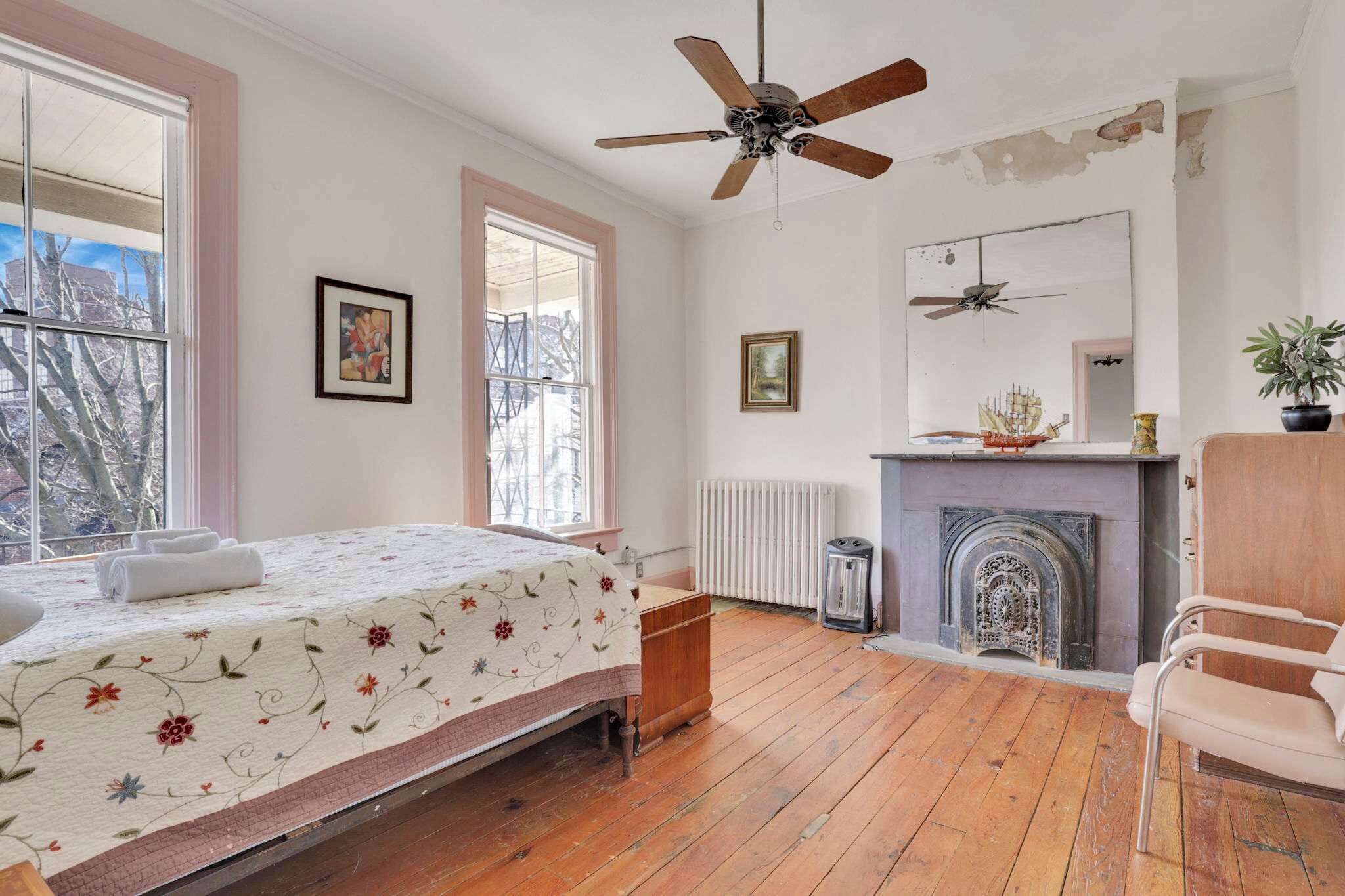 A bedroom with a bed, a ceiling fan, a fireplace, and a window with a view of trees.