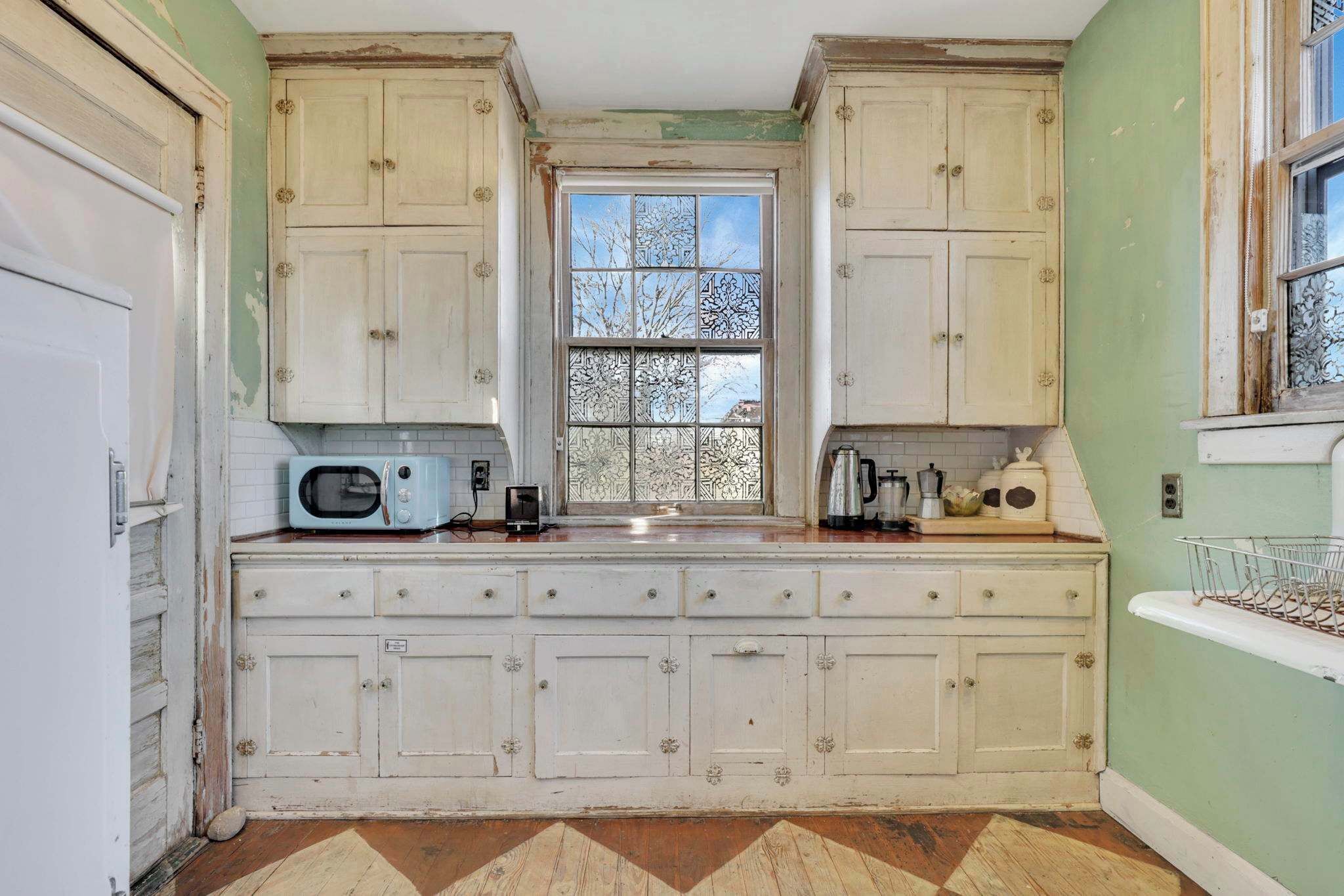 A kitchen with white cabinets, a window with a view, and a microwave on the counter.