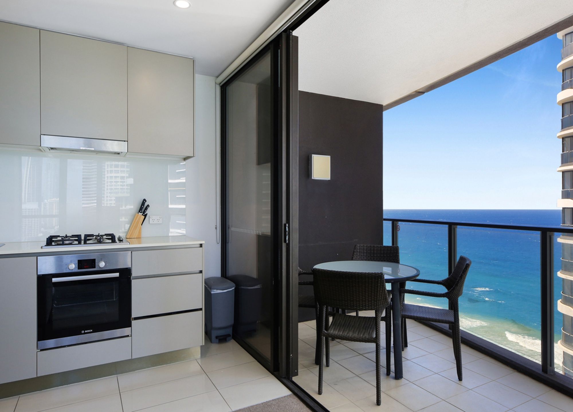 A modern kitchen with a Bosch oven, a dining area with a table and chairs, and a balcony with a view of the ocean.