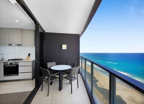 A balcony with a view of the ocean, a dining table with chairs, and a kitchen area.