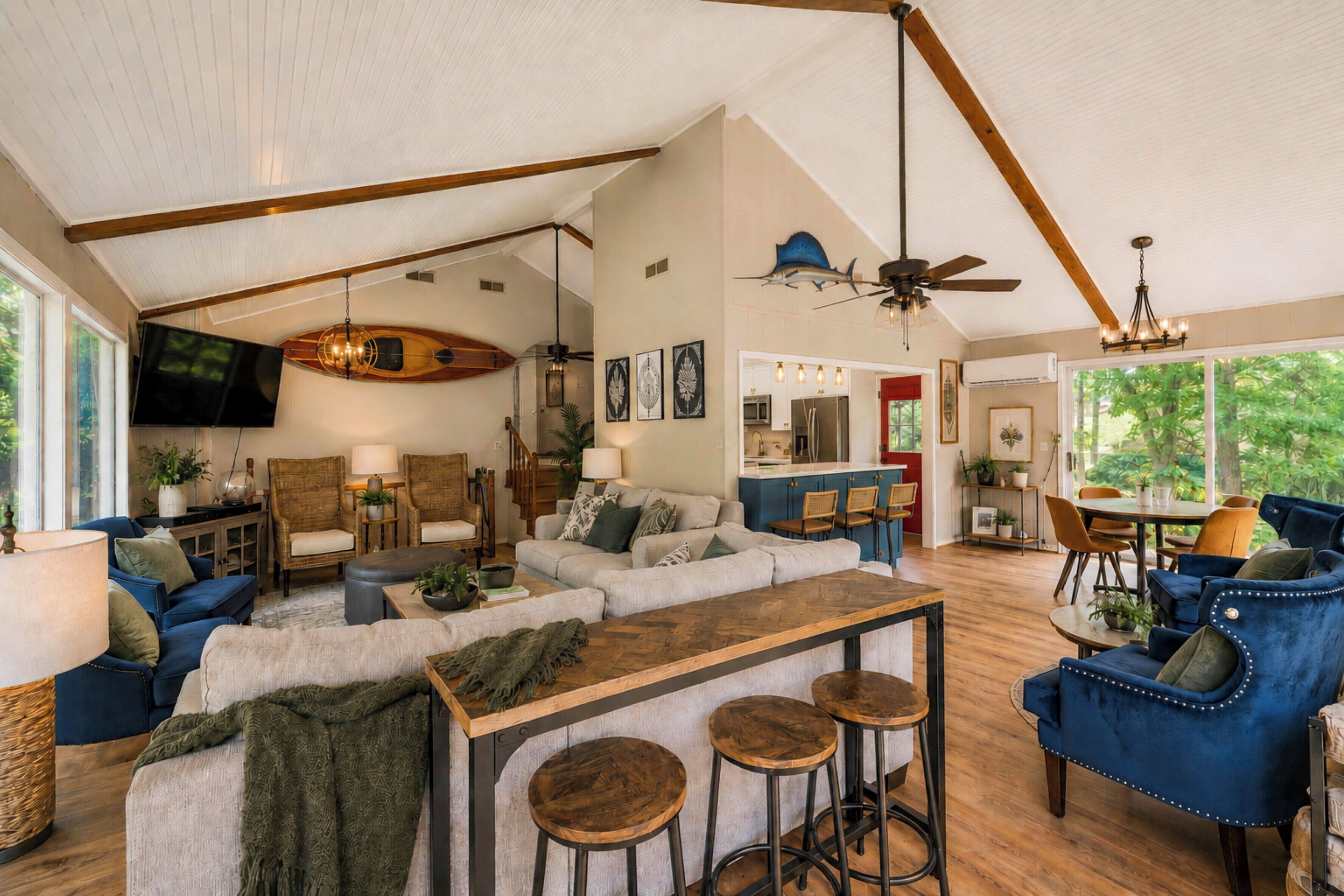 A spacious living area with a wooden ceiling, a large sofa, a dining table, and a kitchen in the background.