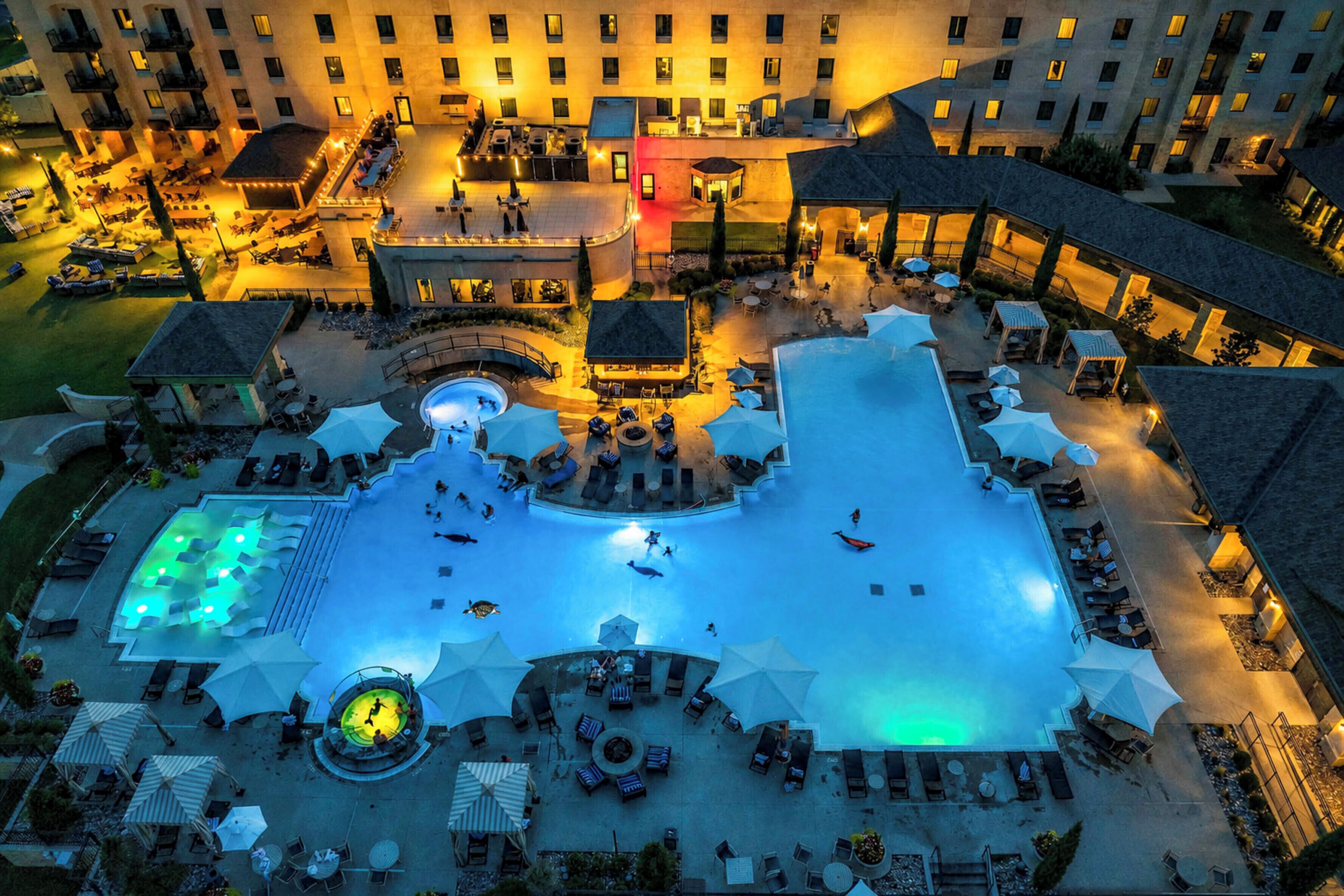 Vue aérienne d’un hôtel doté d’une piscine centrale, d’espaces de détente en plein air et de plusieurs bâtiments.