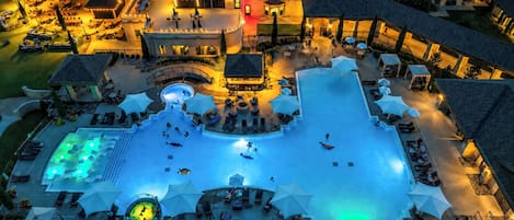 Eine Vogelperspektive zeigt ein Hotel mit einem zentralen Schwimmbecken, Sitzgelegenheiten im Freien und mehreren Gebäuden.