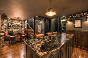 Un espace bar avec un mur en pierre, des tabourets de bar en bois et un comptoir en granit.