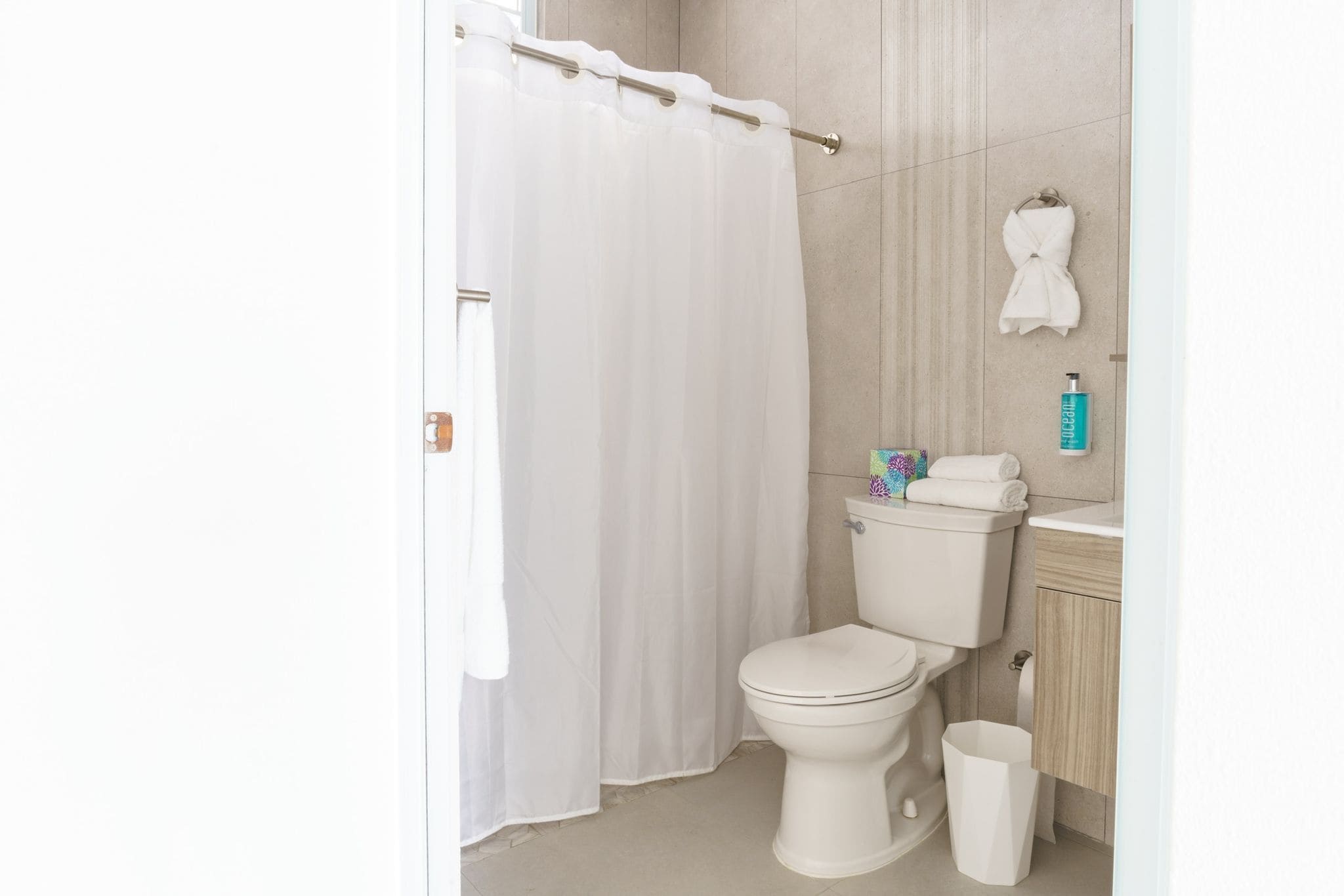 Een badkamer met een toilet, douchegordijn, wastafel en een prullenbak.
