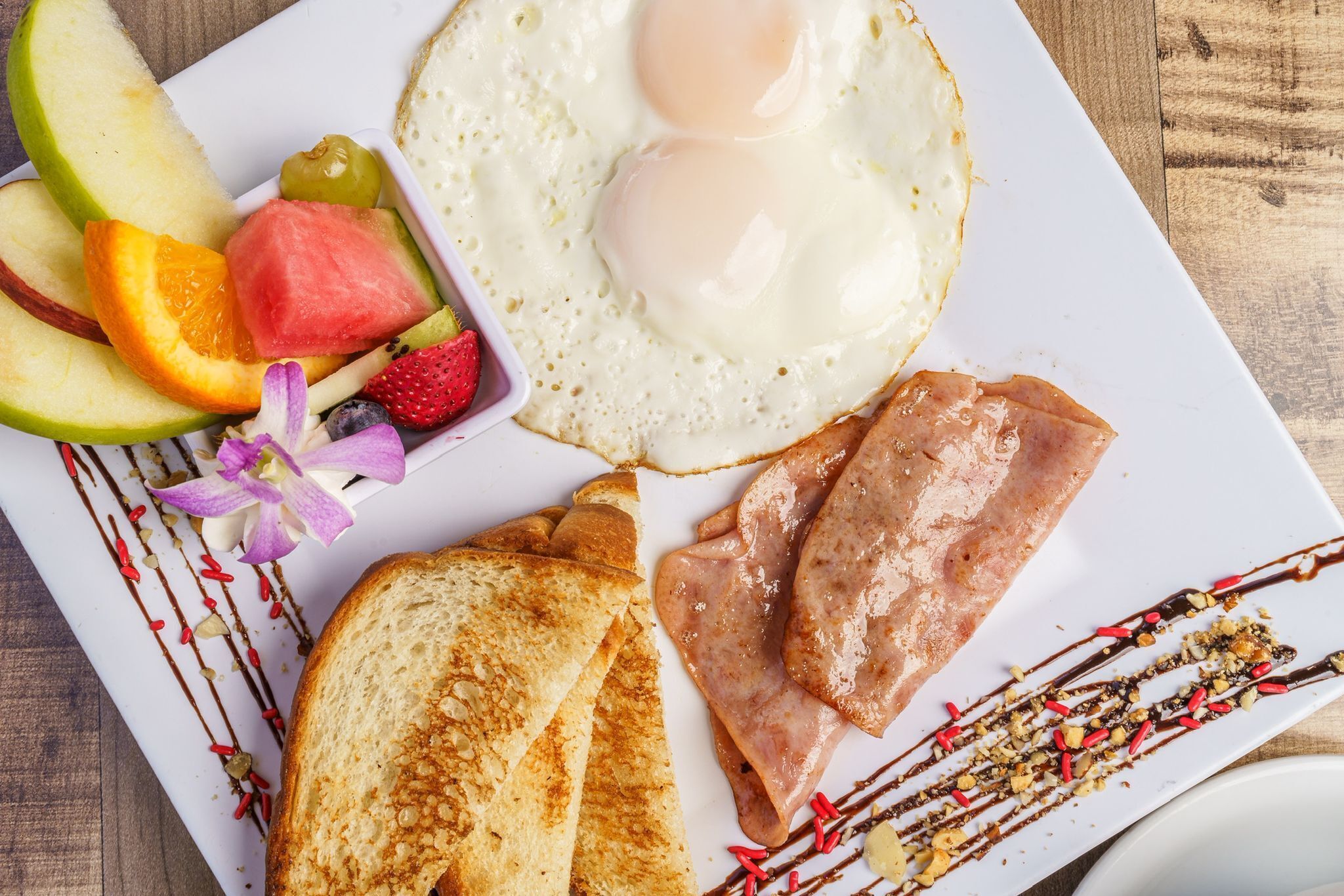 Een ontbijt bord met eieren, toast, ham en fruit.