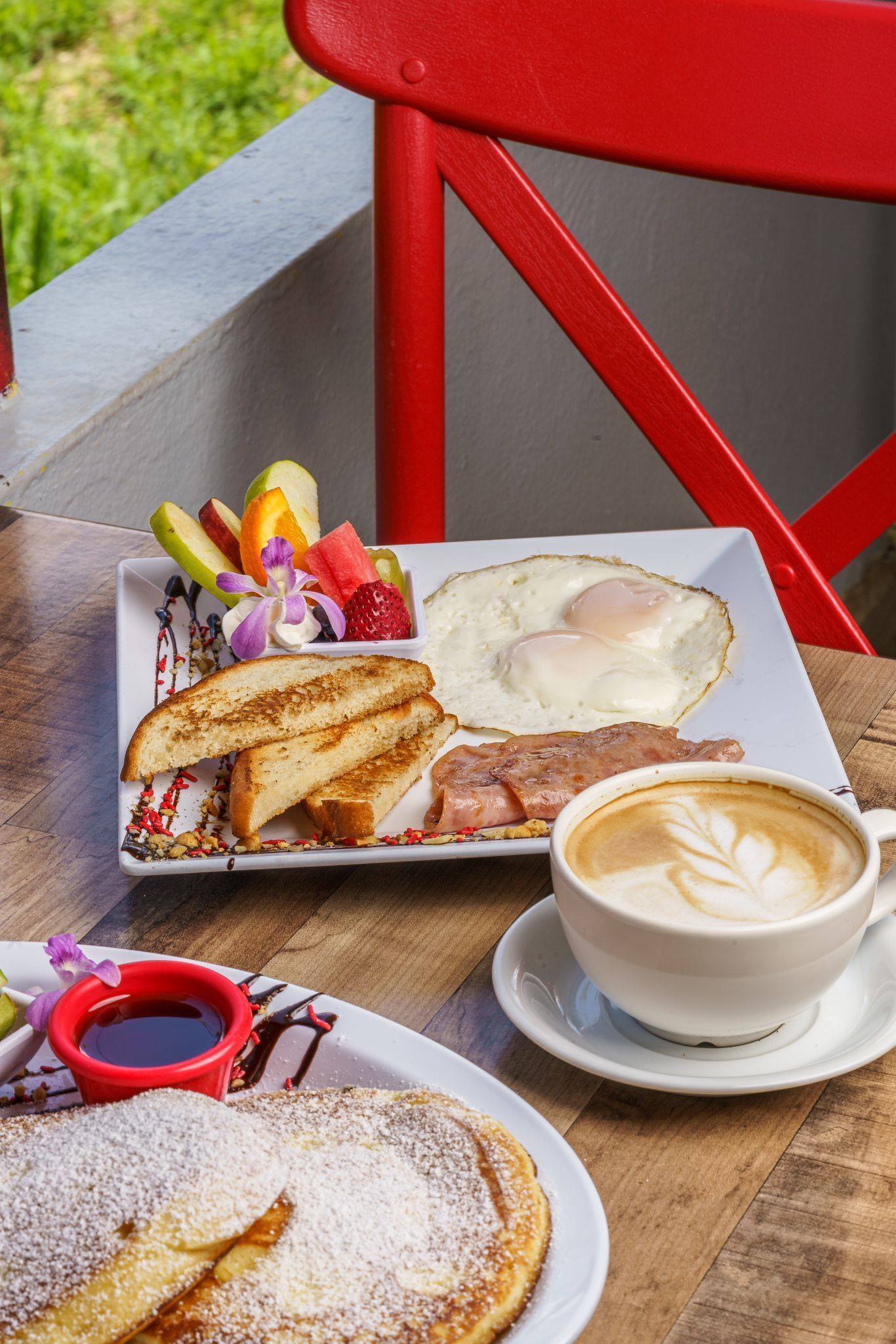 Prato de café da manhã com torradas, ovos, frutas, uma xícara de café e uma caneca vermelha de xarope.