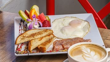 Un plato de desayuno con tostadas, huevos y fruta, una taza de café y una taza roja de almíbar.