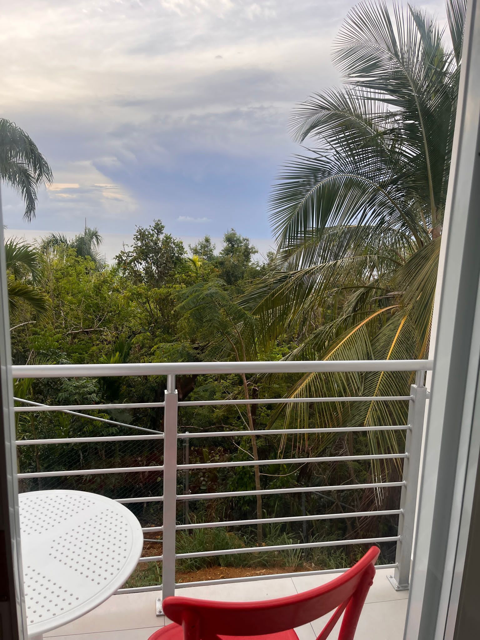 A balcony with a white metal railing, a white table, and a red chair.