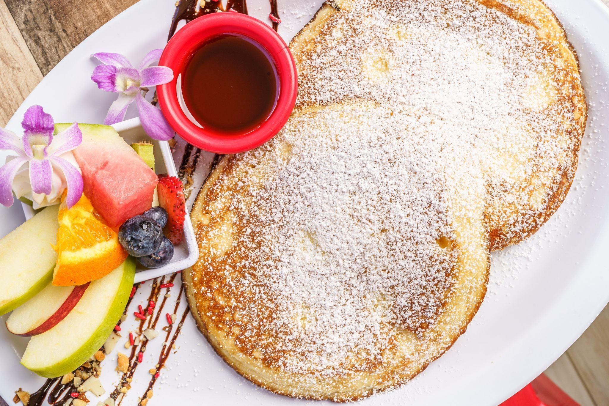 A plate with pancakes, fruit, and syrup.