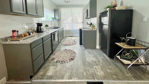 A modern kitchen with grey cabinets, a black refrigerator, and a small island with a sink. There are two rugs on the floor and a ceiling light fixture. - Charming Retreat | Walkable • Private Fenced Yard (Indianapolis)