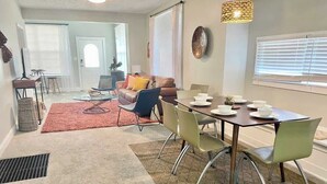 A modern living room with a dining area, featuring a sofa, a coffee table, and a dining table with chairs. - Charming Retreat | Walkable • Private Fenced Yard (Indianapolis)