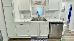 A modern kitchen with white cabinetry, a double sink, and a dishwasher. - Newly Remodeled 2 Bedroom Home in Shelbyville! (Shelbyville)