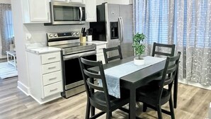 A modern kitchen with white cabinets, a stainless steel refrigerator, an oven, and a microwave. There is a dining table with chairs and a small potted plant on the table. - Newly Remodeled 2 Bedroom Home in Shelbyville! (Shelbyville)