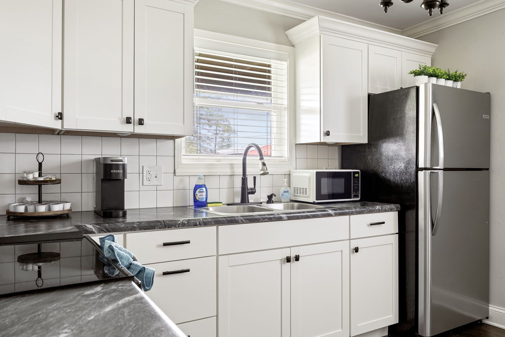 A modern kitchen with white cabinets, a stainless steel refrigerator, a microwave, and a coffee maker.