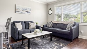 Una sala de estar con dos sofás gris oscuro, una mesa de centro blanca y un tapete negro.