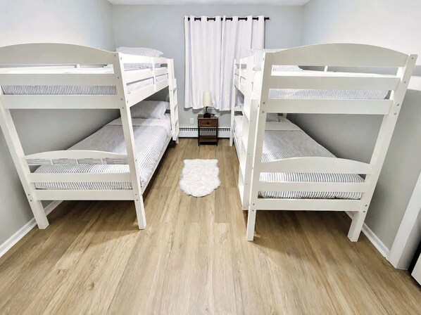 A room with two bunk beds, a small table with a lamp, and a white fur rug on the floor.