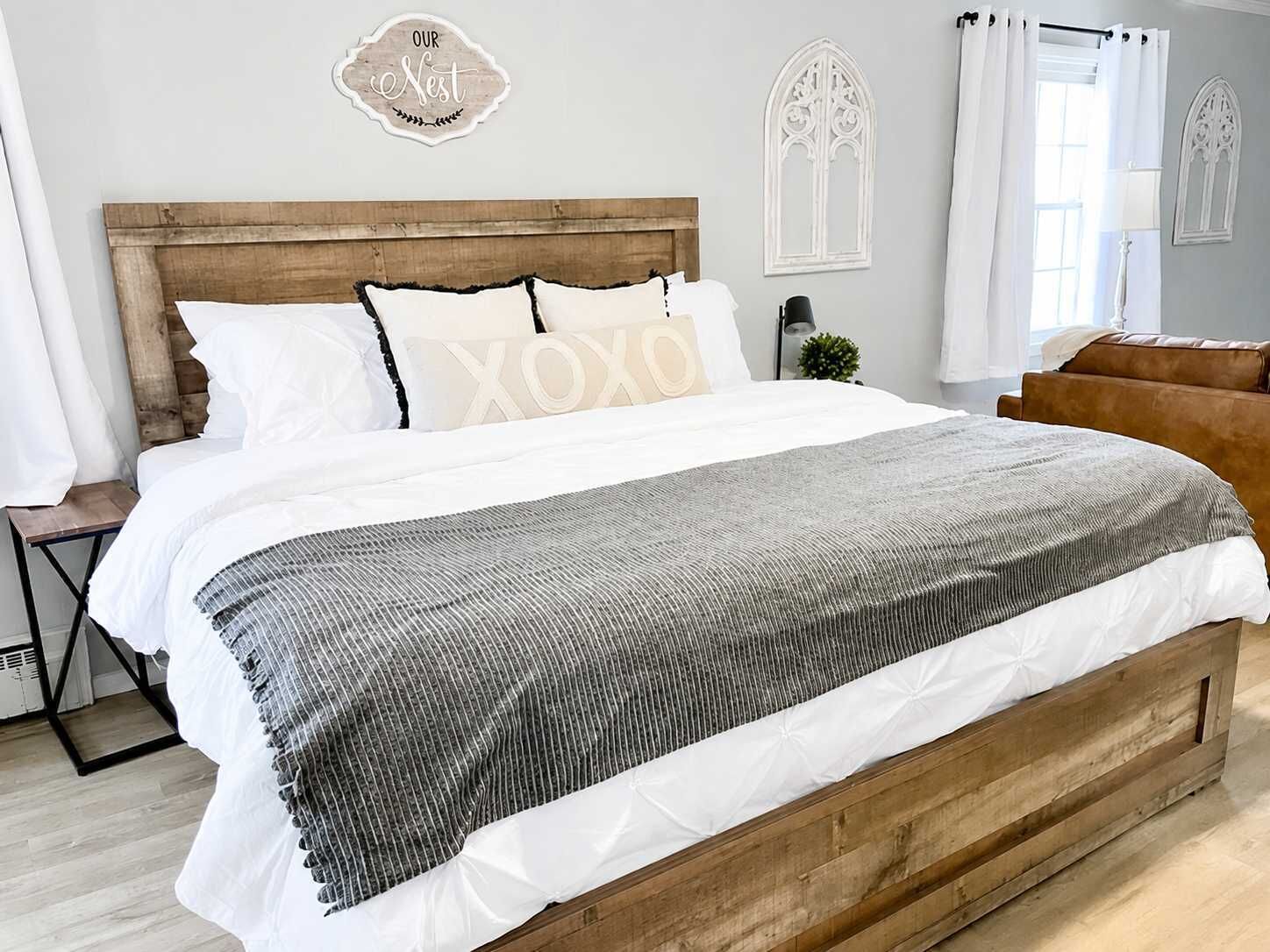 A bedroom with a wooden headboard, white bedding, and a grey patterned throw.