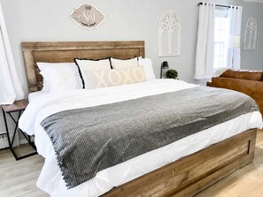 A bedroom with a wooden headboard, white bedding, and a grey patterned throw. - Spacious Ivy Hills Home | Hot Tub • Fenced Yard (Indianapolis)