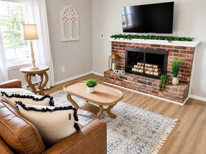 A living room with a fireplace, a television mounted above it, and a cozy seating area with a couch and a coffee table. - Spacious Ivy Hills Home | Hot Tub • Fenced Yard (Indianapolis)