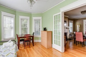 Una habitación con cama, escritorio, silla y cómoda. Hay ventanas con persianas, un ventilador de techo y una puerta que da a otra estancia.