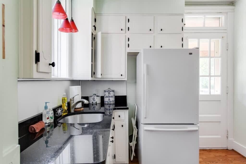 A kitchen with white cabinets, a black countertop, a white refrigerator, and a window with blinds.