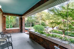A covered outdoor area with brick walls, a swing, and a view of a street with cars and trees.