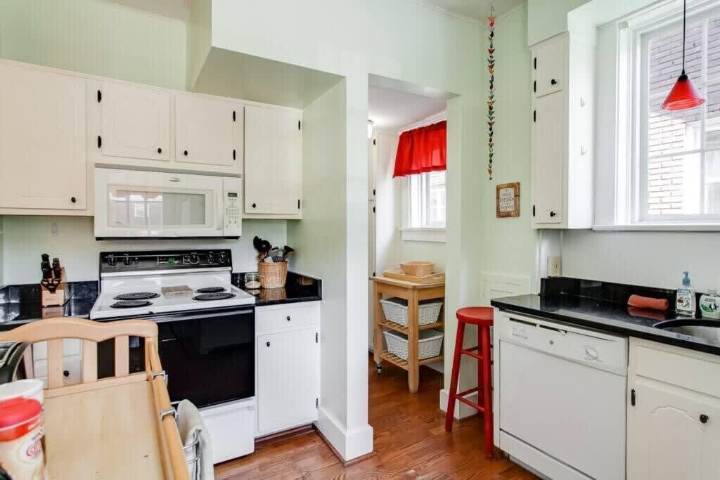 A compact kitchen with white cabinets, a microwave, stove, and a red hanging light fixture.