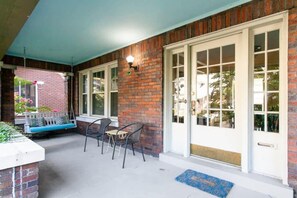 A covered patio with a brick wall, white-framed glass doors, and a seating area with a bench and chairs.