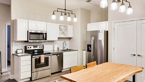 A modern kitchen with white cabinetry, stainless steel appliances, and a wooden dining table. - Theatre District Condo | Gym • Free Parking • DT (Louisville)