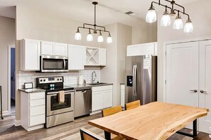 A modern kitchen with white cabinetry, stainless steel appliances, and a wooden dining table.