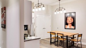 A modern kitchen with a wooden dining table and chairs, a refrigerator, and a pendant light fixture. - Theatre District Condo | Gym • Free Parking • DT (Louisville)