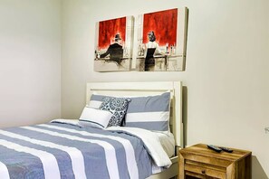 A bed with striped bedding, a bedside table with a remote, and two wall-mounted paintings.