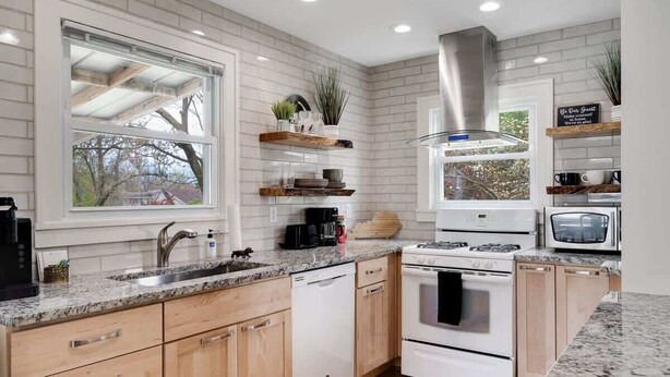 Una cocina moderna con armarios blancos, encimeras de granito, una campana extractora de acero inoxidable y estantes empotrados.