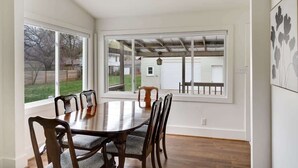 Un comedor con mesa y sillas de madera, ventanas amplias y vista al patio trasero.
