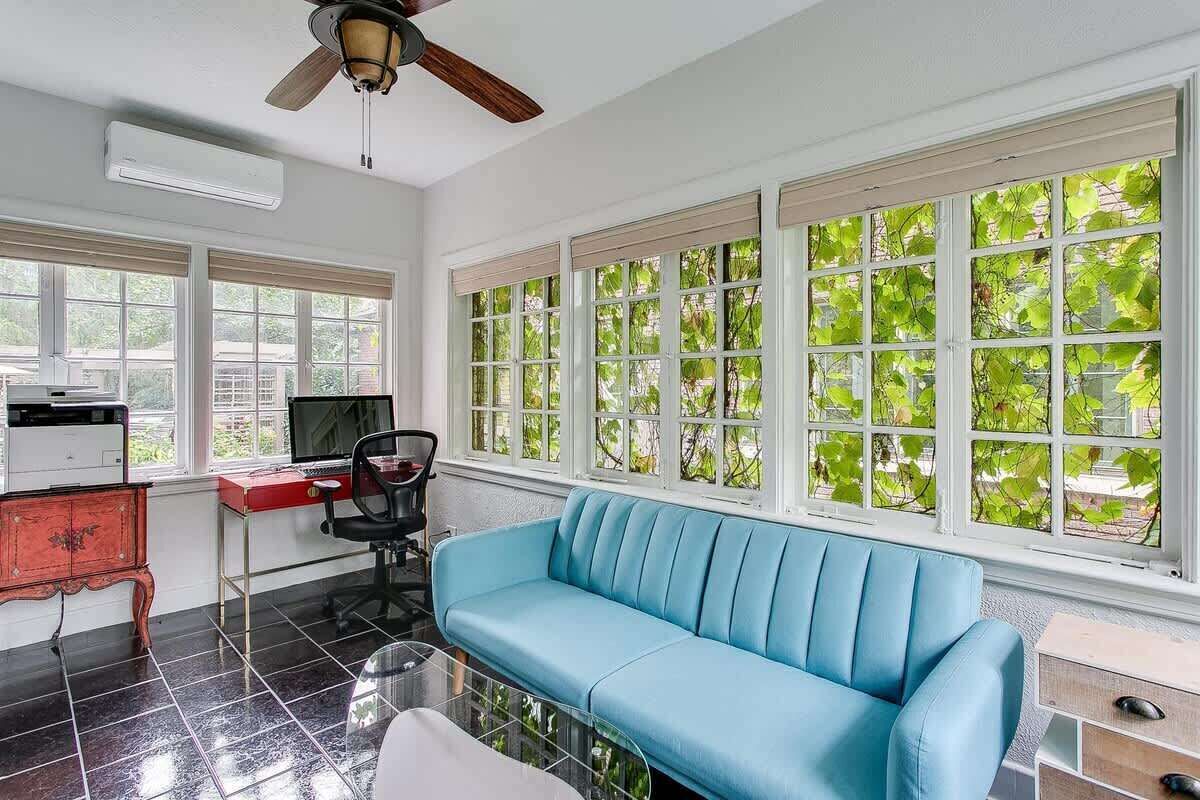 A room with a blue sofa, a desk with a computer, and a ceiling fan.