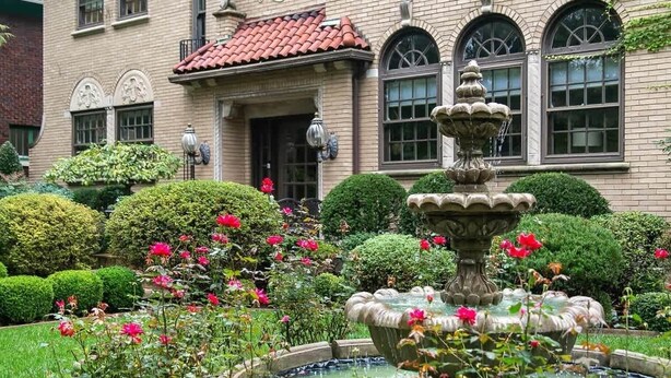 Un edificio histórico con una fuente, jardines cuidados y un tejado de tejas rojas.