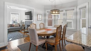 A dining area with a round table, six chairs, and a hanging light fixture.