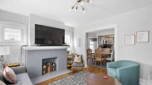 A modern living room with a fireplace, a television mounted above it, and a dining area in the background.
