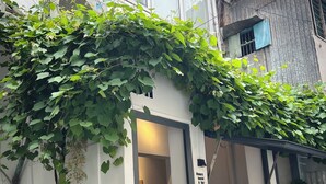 A building with a white exterior, a wooden bench, and a doorway leading inside. - 8h - Hostel  (Ho Chi Minh City)