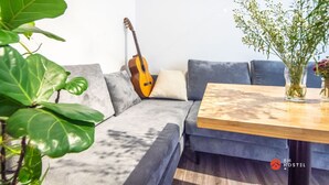 A modern living room with a grey sofa, a wooden coffee table, a guitar leaning against the wall, and a large green plant. - 8h - Hostel  (Ho Chi Minh City)