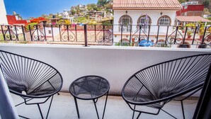A balcony with three black wire-framed chairs and a small table, overlooking a residential area with terracotta-roofed houses and a hill in the background. - Beautiful Casa Madero 470 (Puerto Vallarta)