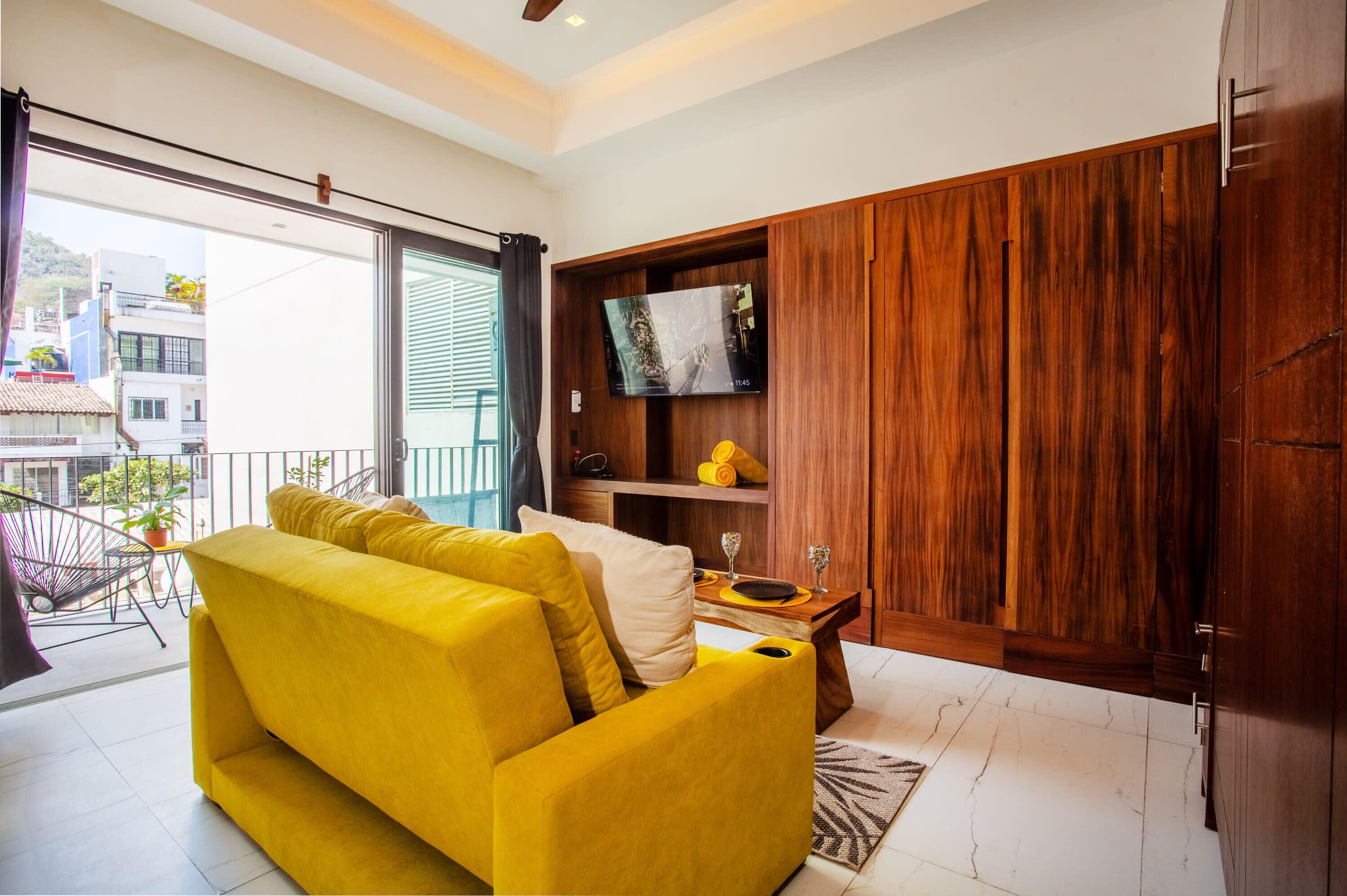 A living room with a yellow sofa, a wooden cabinet, and a television on the wall.