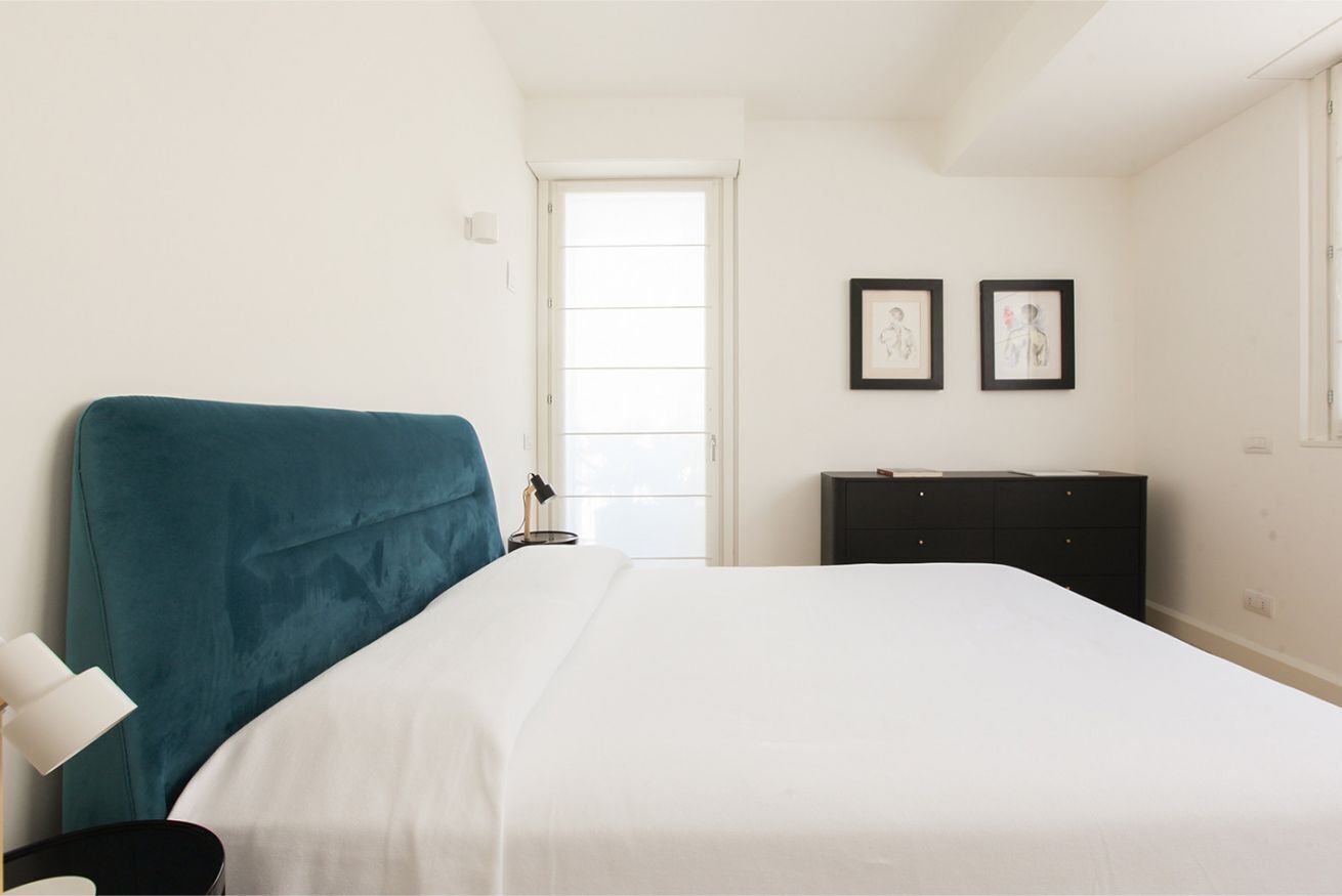 A bedroom with a teal headboard, white bedding, a black dresser, and two framed pictures on the wall.