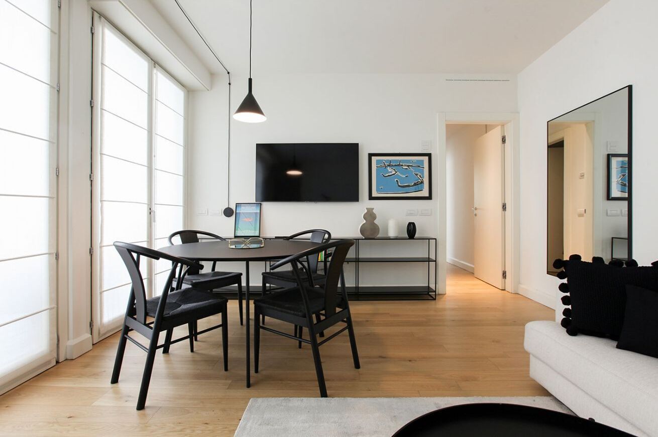 Een moderne woonkamer met een eethoek, een flatscreen televisie aan de muur en een grote spiegel die de kamer weerkaatst.