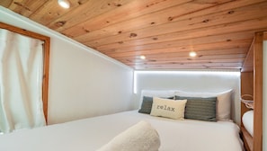 Un dormitorio con techo de madera, ropa de cama blanca y una almohada con la etiqueta 'relax'.
