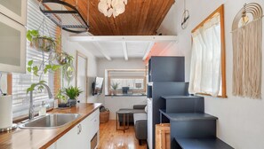 Una cocina moderna con encimera de madera, pileta de acero inoxidable y plantas colgantes. Se observa una escalera con acabado oscuro que conduce a una zona de descanso.