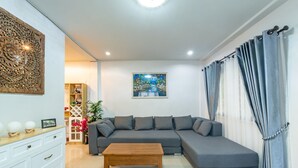 A modern living room with a grey sectional sofa, a wooden coffee table, a white cabinet, and a painting on the wall. - Spacious 3BR Private House Near Old City Near Night Bazaar (Muang Chiang Mai)