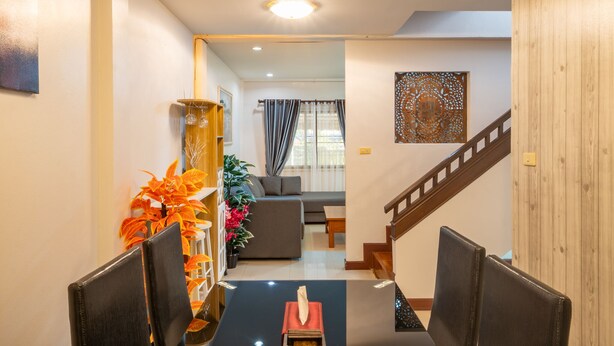 A modern living room with a sofa, a dining area with chairs, a staircase, and a decorative wall piece. - Spacious 3BR Private House Near Old City Near Night Bazaar (Muang Chiang Mai)