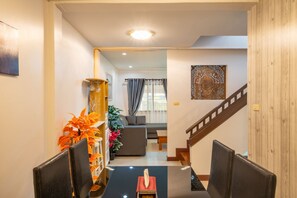 A modern living room with a sofa, a dining area with chairs, a staircase, and a decorative wall piece.